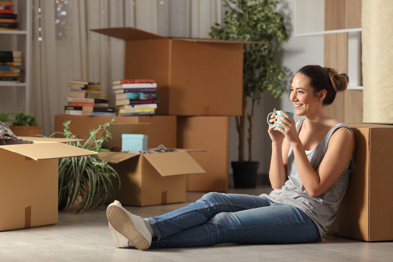 Happy tenant resting drinking coffee moving home sitting on the floor in the night